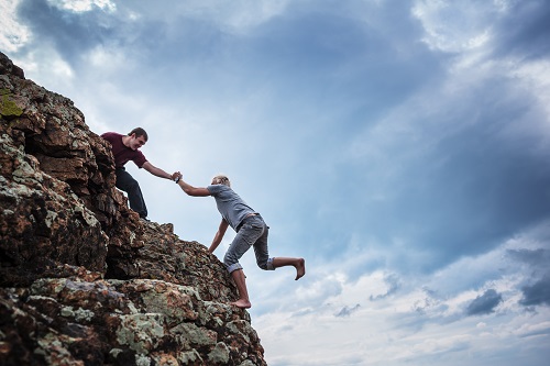 Men helping each other climb a rock.